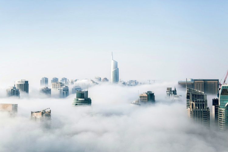 How To Build iOS Apps Without A Mac. An image of the tops of buildings of a cityscape. The building tops are shrouded in clouds.